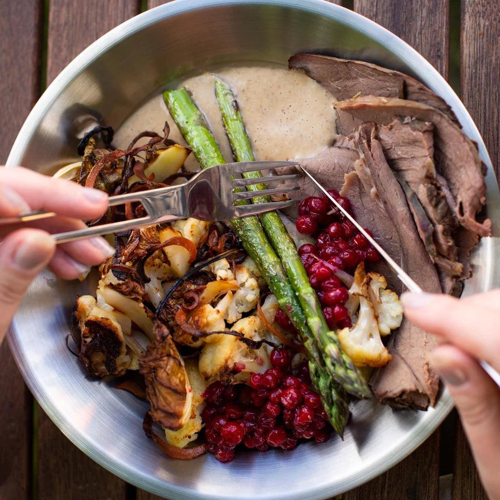 Outdoor metal bowl with roast beef, asparagus, cauliflower, lingonberries, brown sauce