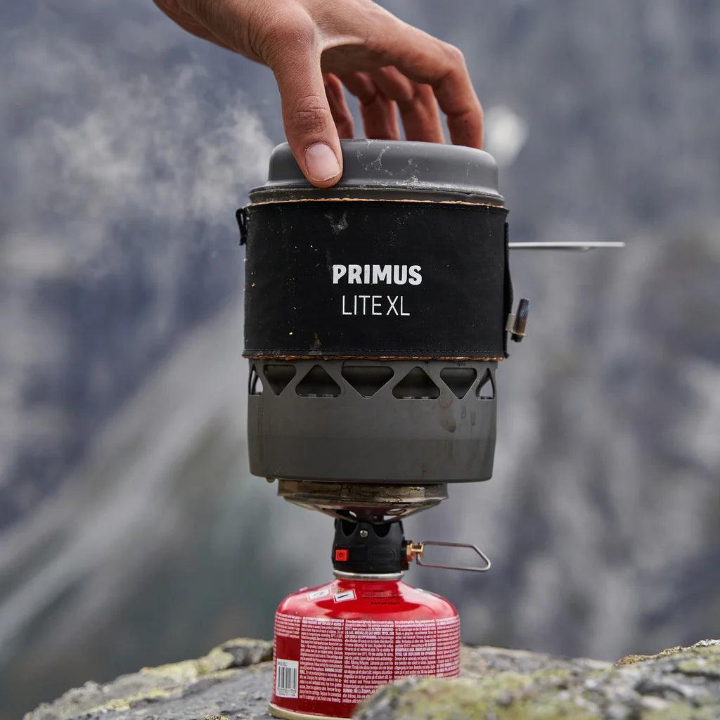 Primus Lite XL camping stove system on rock outdoors, mountain background, hand adjusting lid