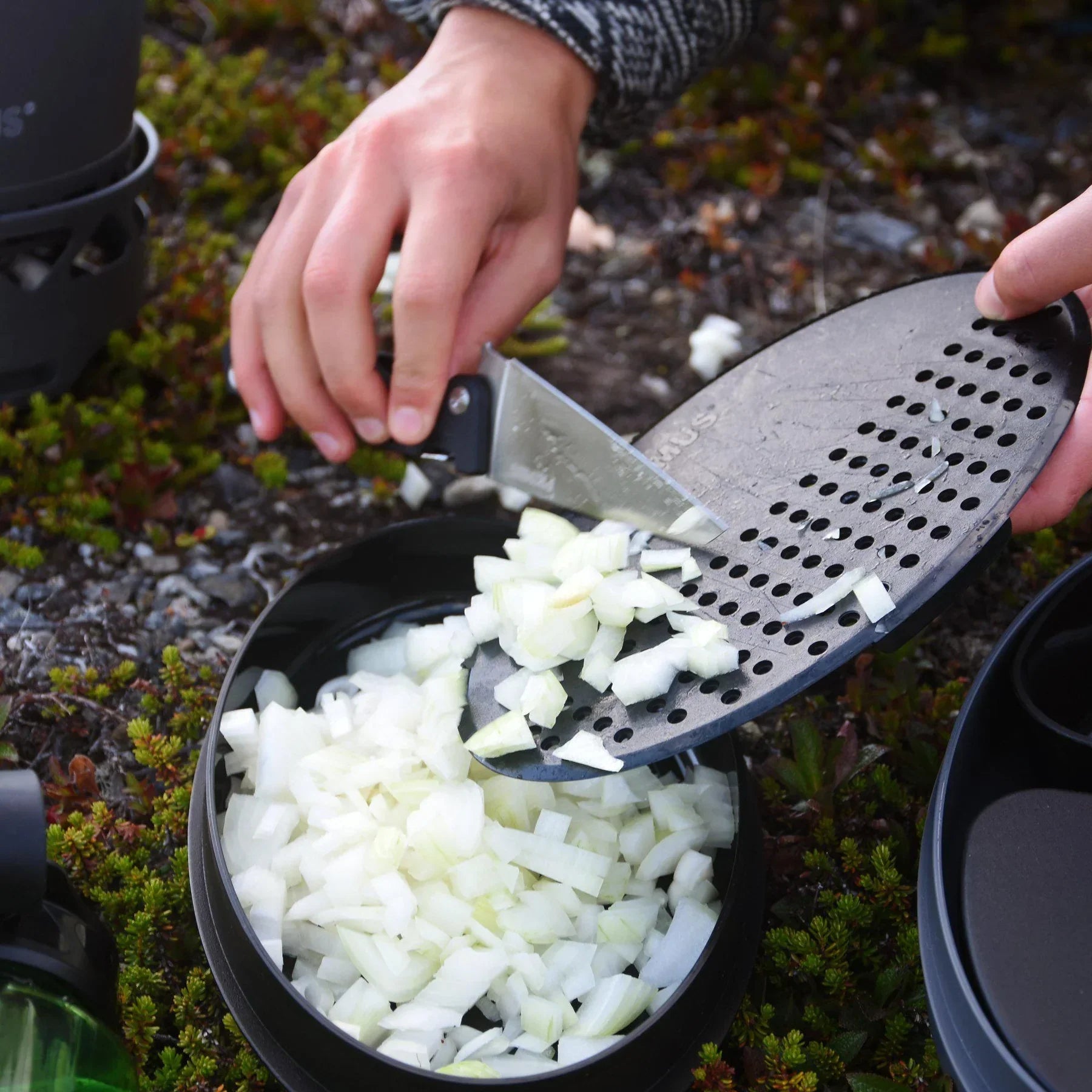 Chopped onions being transferred into a black camping bowl outdoors