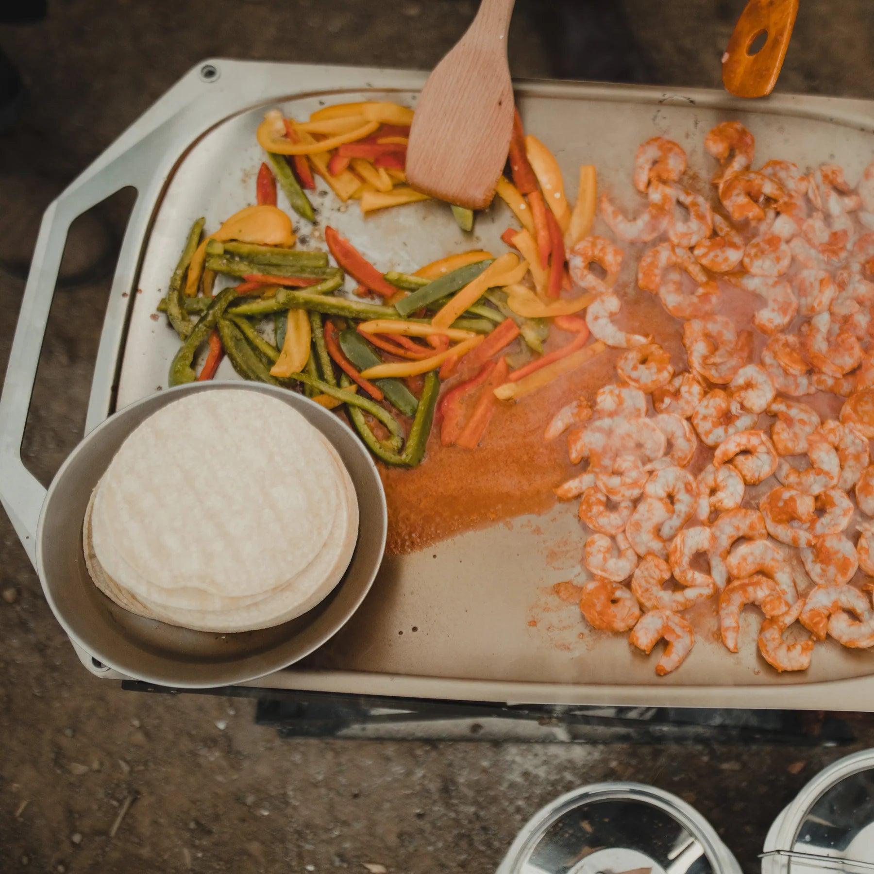 Grilled shrimp, sliced peppers, and tortillas on Primus OpenFire pan outdoors
