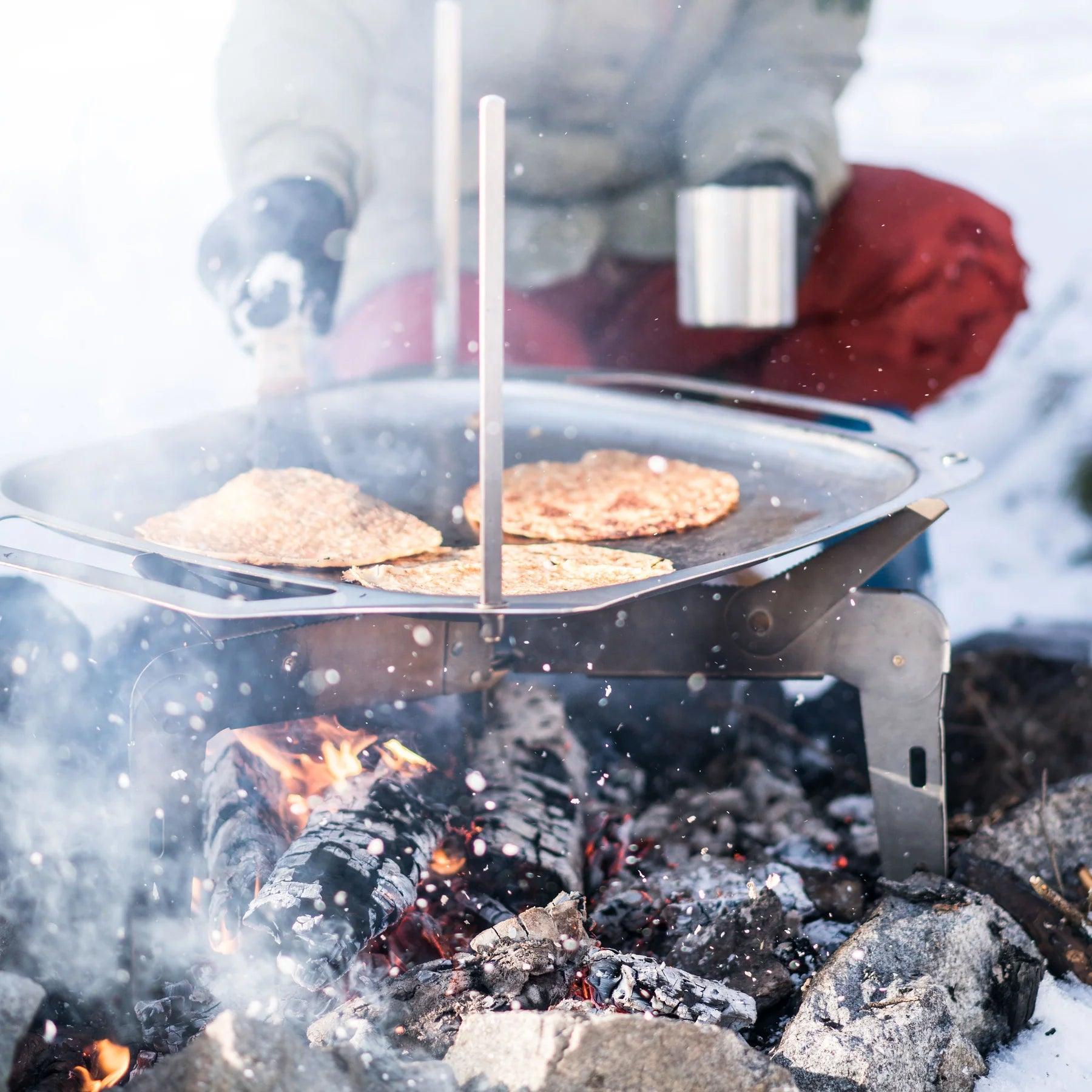 Primus OpenFire Pan cooking pancakes over campfire outdoors in snowy setting