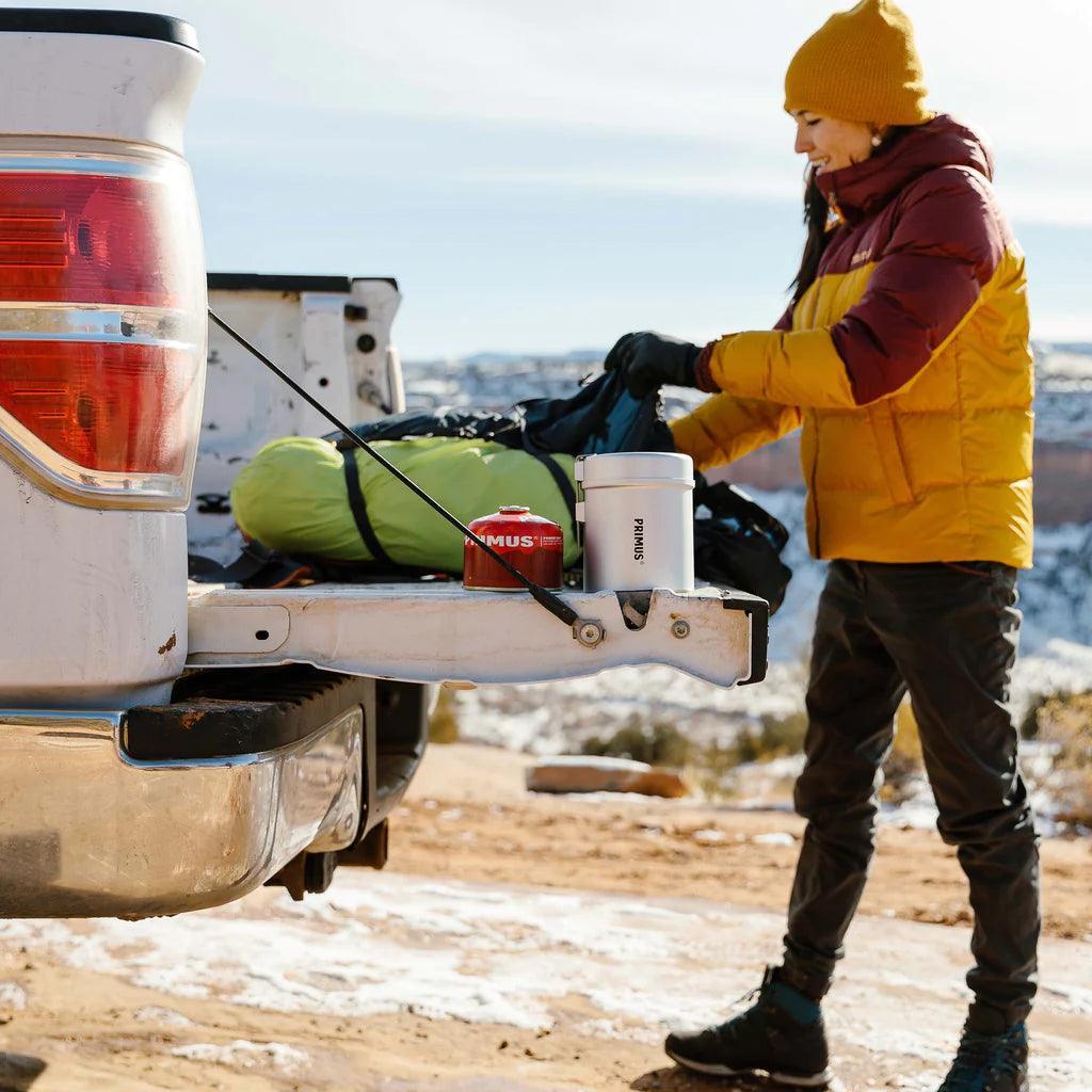 Camper packing gear by truck with Primus gas canister and stove outdoors in winter