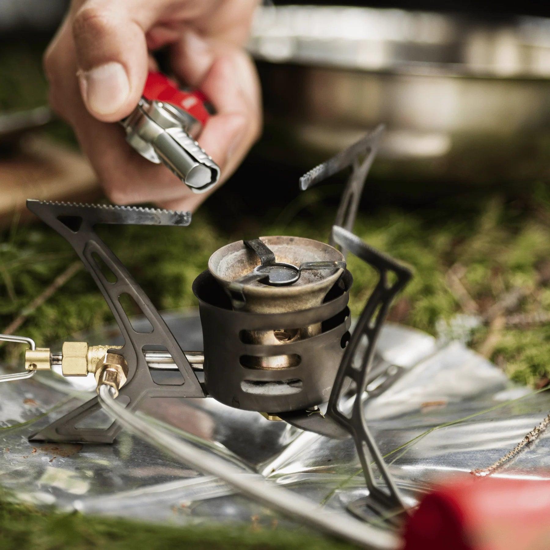 Hand using power lighter to ignite portable camping stove on grass