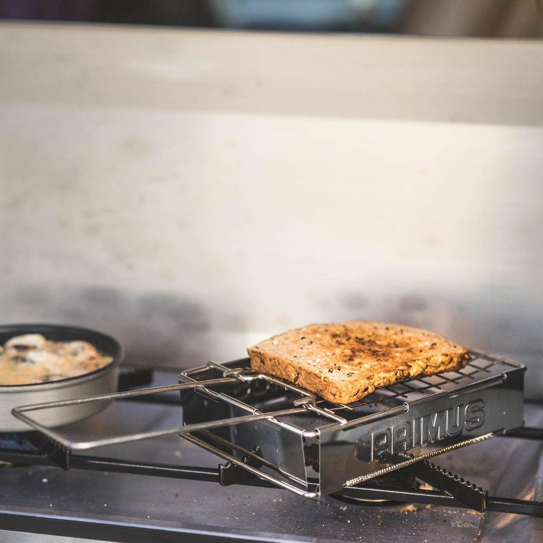 Primus toaster toasting bread on a portable outdoor stove, camping cookware in use