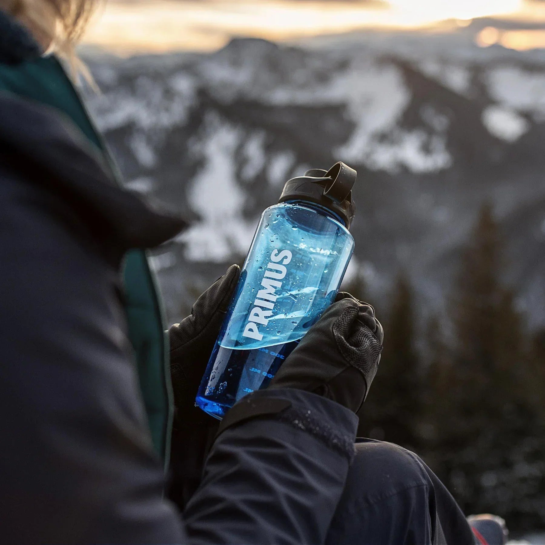 Person holding a blue Primus trail bottle outdoors with snowy mountain background