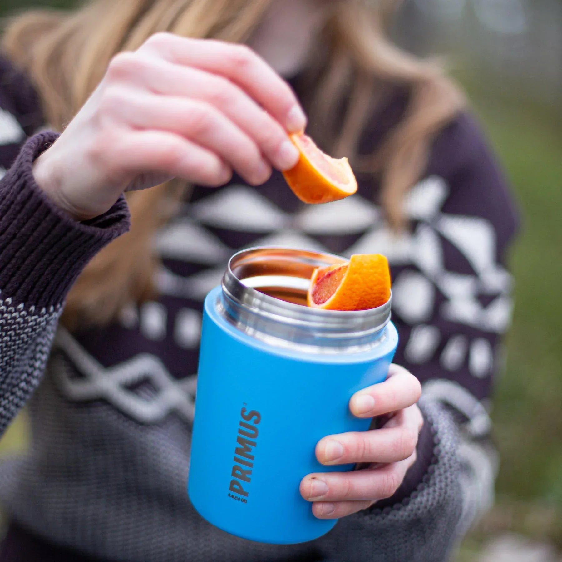 Person adding orange slices to blue Primus lunch jug outdoors