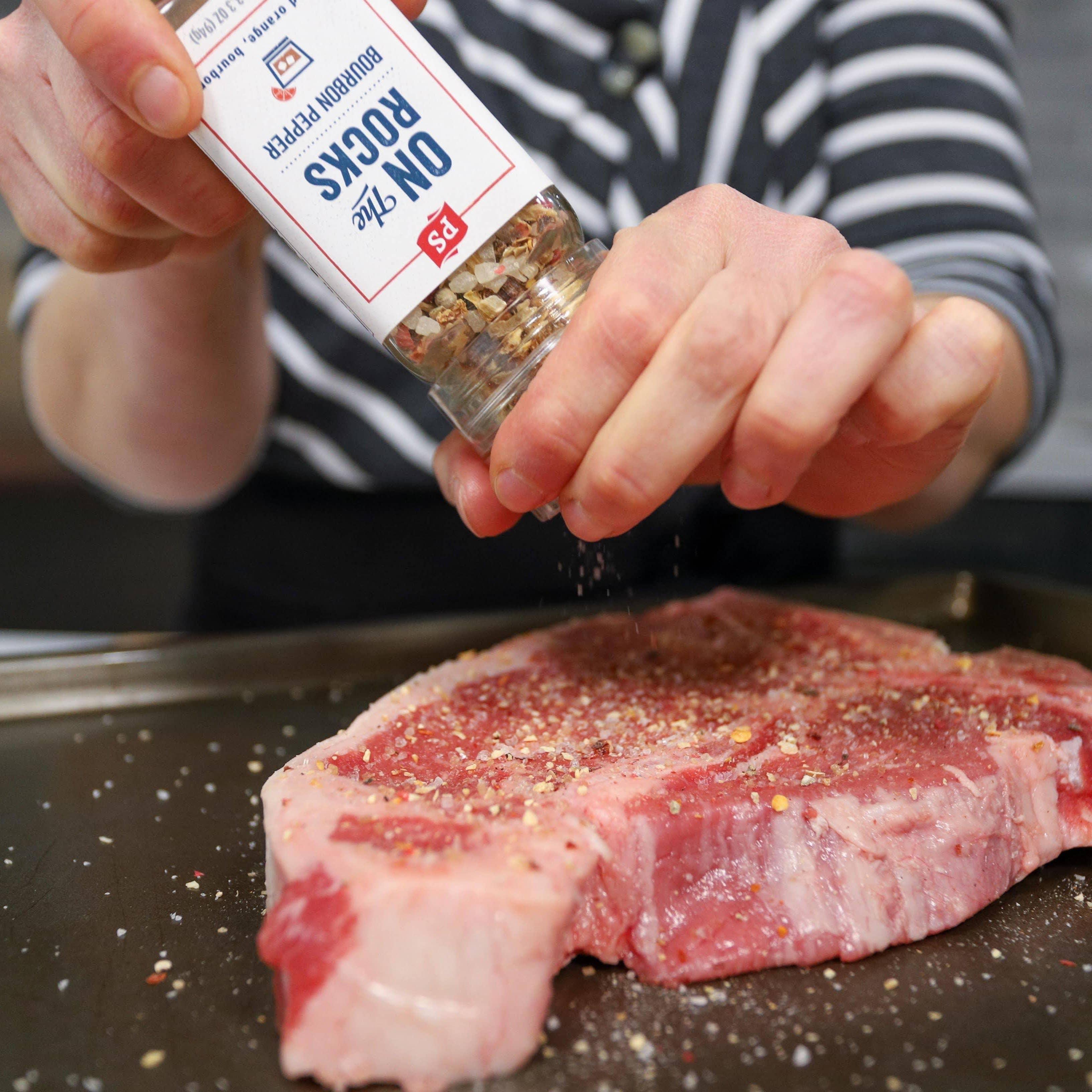 Seasoning raw steak with PS Seasoning On the Rocks Bourbon Pepper grinder