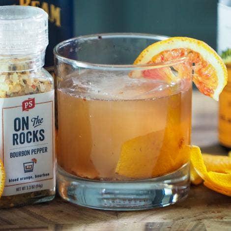 On The Rocks bourbon pepper grinder beside a bourbon cocktail garnished with orange peel