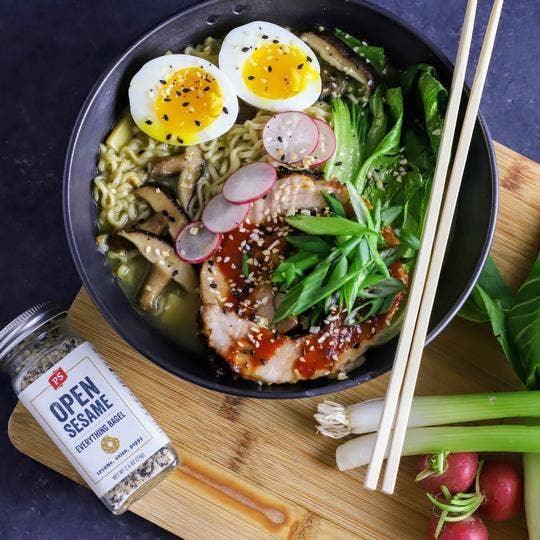 Bowl of ramen topped with soft eggs, pork, vegetables, and PS Seasoning Open Sesame seasoning.