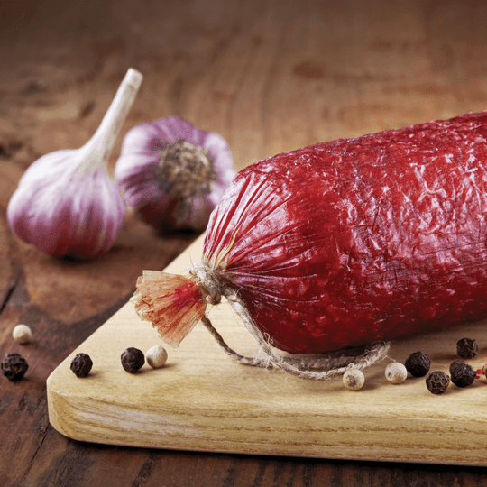 Summer sausage on wooden board with garlic bulbs and peppercorns, rustic setting