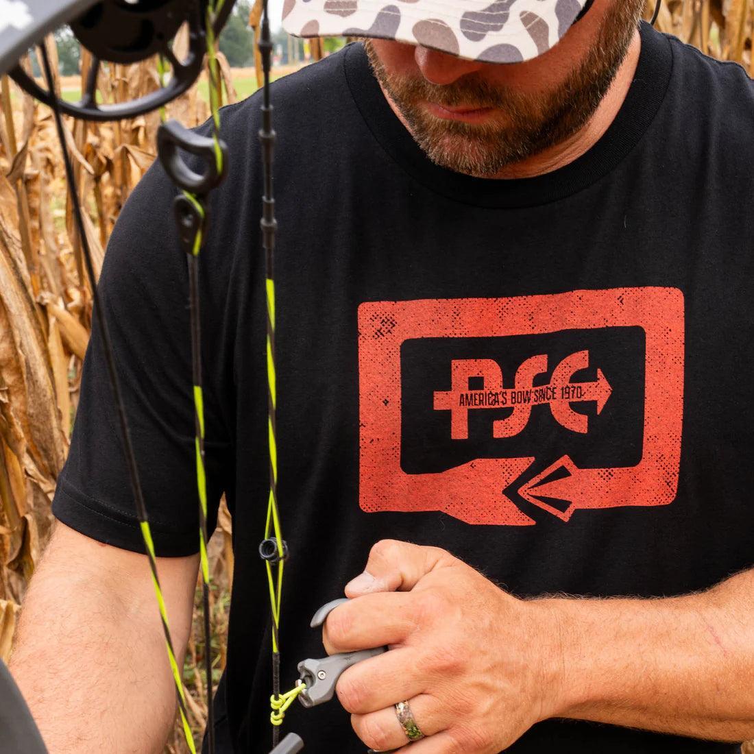Man in PSE Archery T-shirt using compound bow outdoors in cornfield