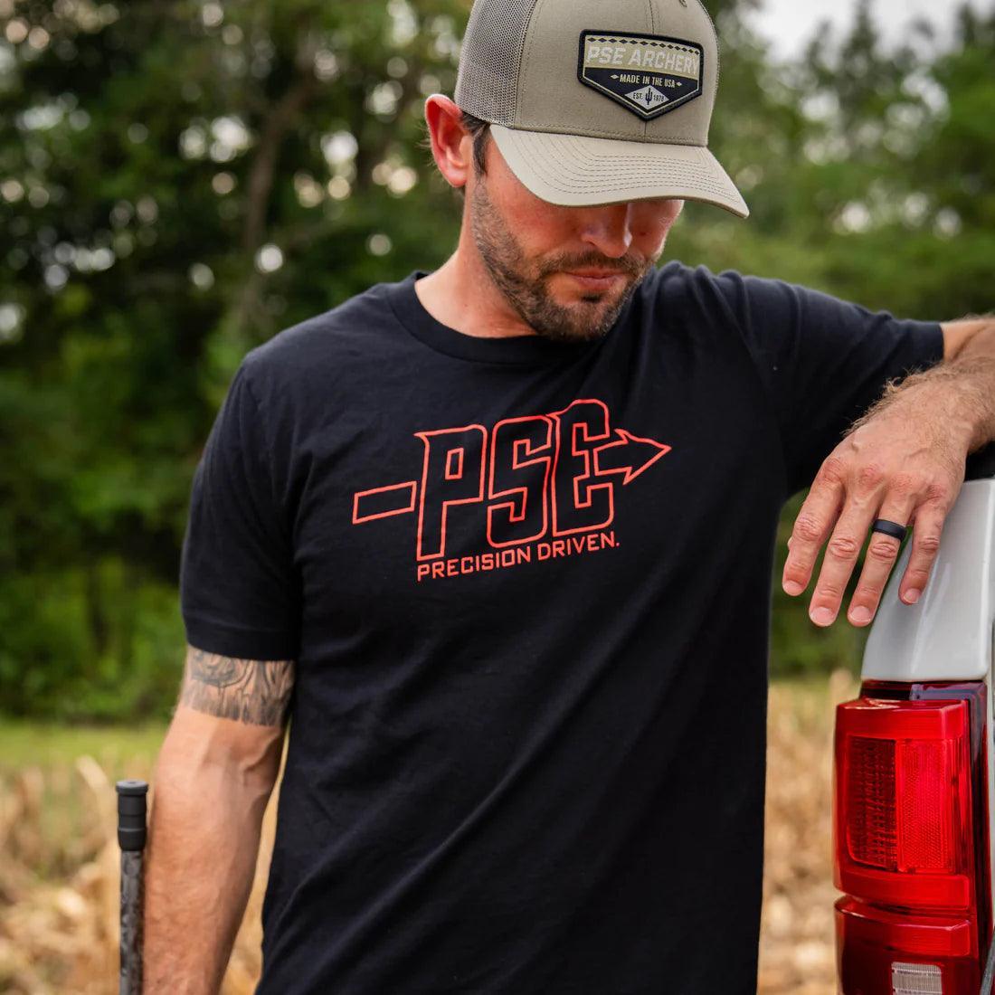 Man wearing PSE Archery logo t-shirt and hat outdoors beside red truck