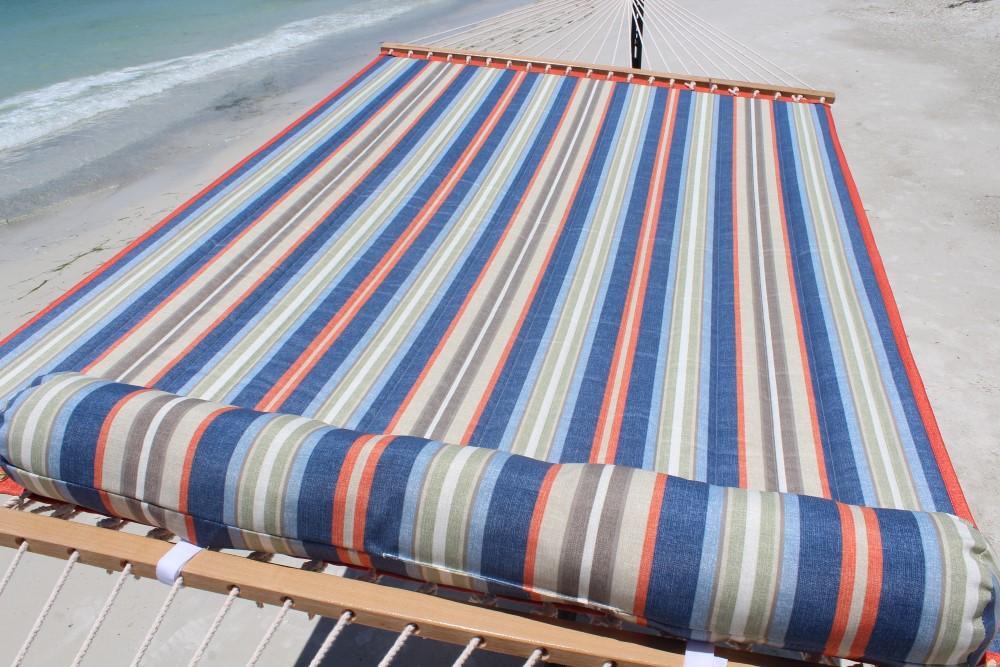 Quilted hammock with blue, red, and grey stripes on a sandy beach by the sea