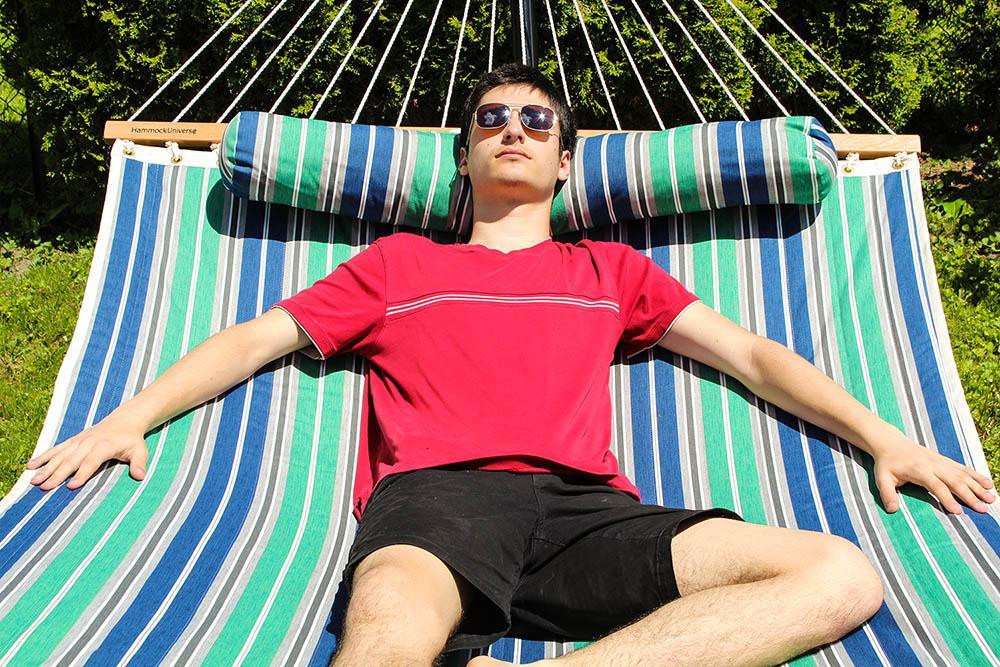 Man relaxing on green and blue quilted double hammock outdoors in sunlight