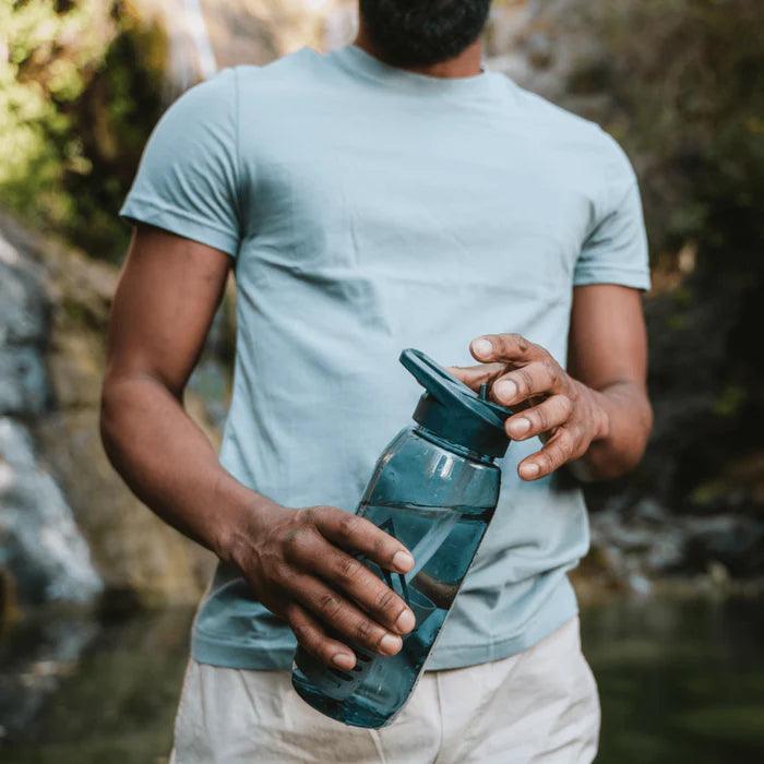 Man holding RapidPure purifier plastic water bottle outdoors near stream