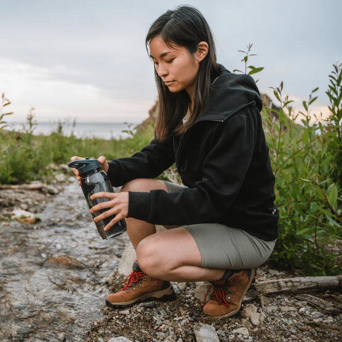 Woman filling RapidPure purifier plastic bottle at a stream during outdoor hiking