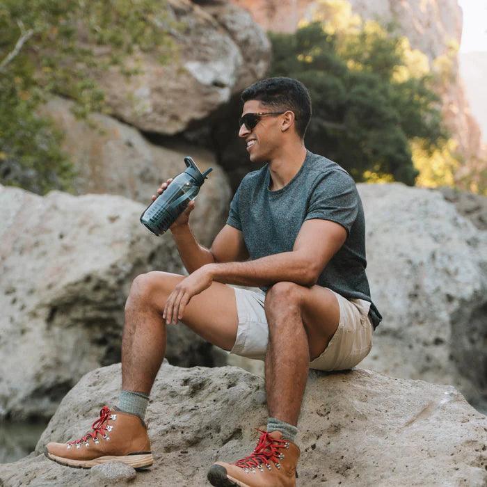 Man hiking outdoors sitting on rock with RapidPure purifier plastic bottle