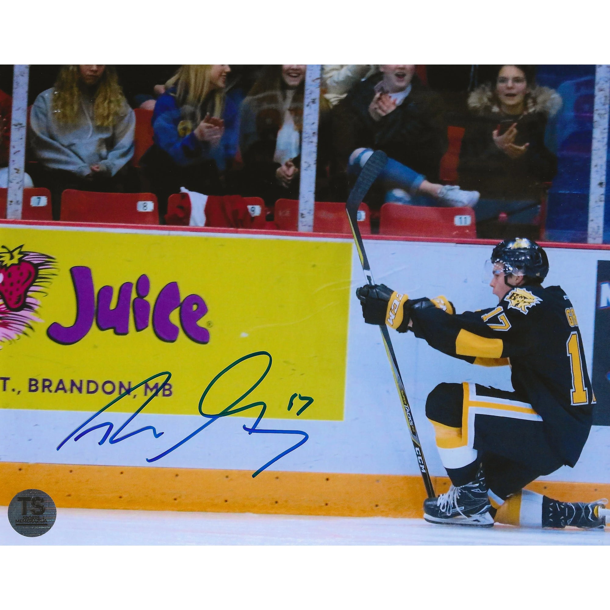 Hockey player in black jersey celebrating on ice near Juice Brandon MB rink ad with fan audience.
