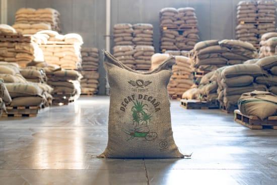 Sack of EA decaf coffee beans in warehouse with stacked burlap coffee bags on pallets
