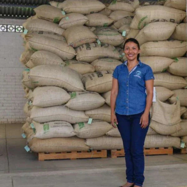 Woman standing by stacked burlap coffee sacks in warehouse