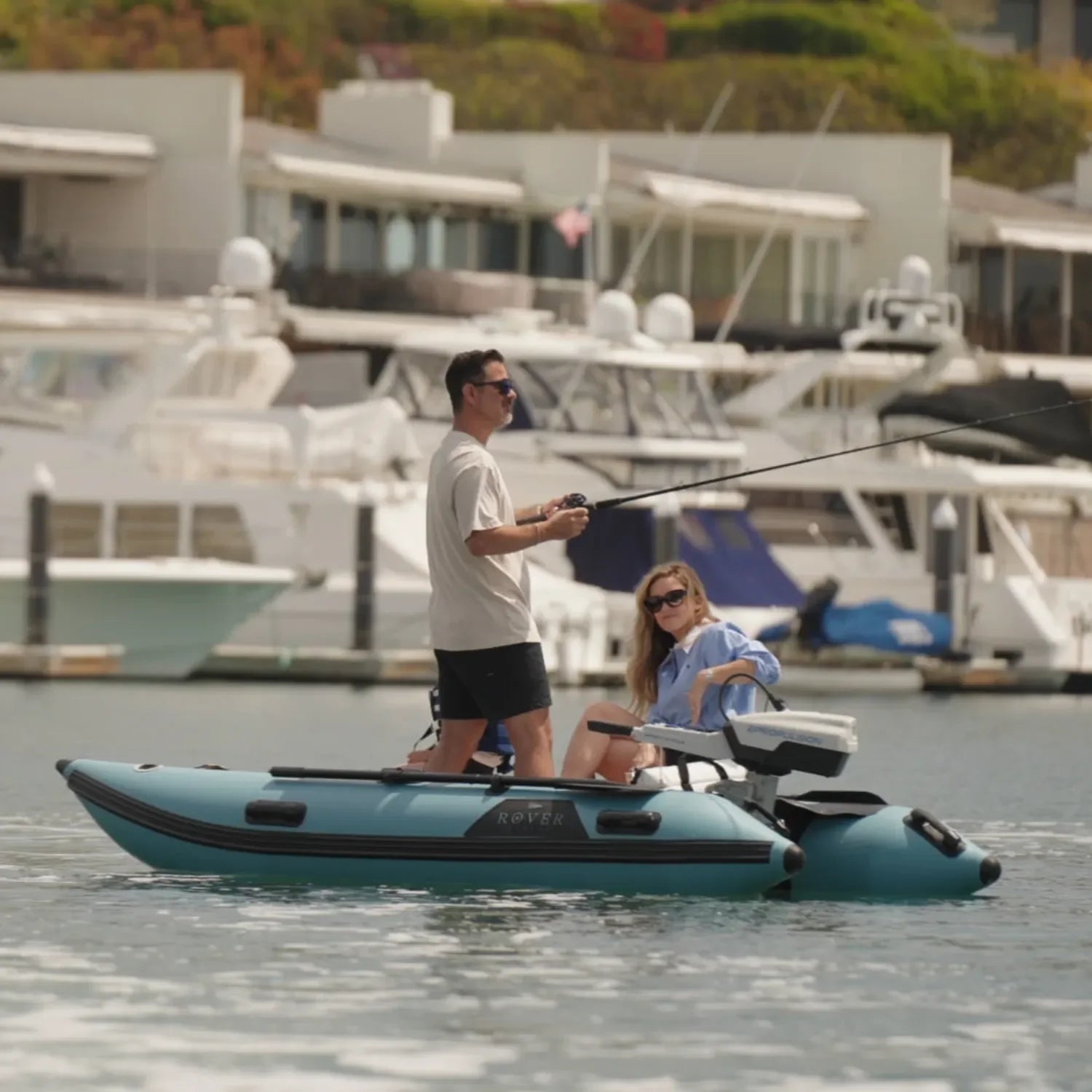 Man and woman fishing on a blue Rover Marine Battle Cat inflatable boat in a marina