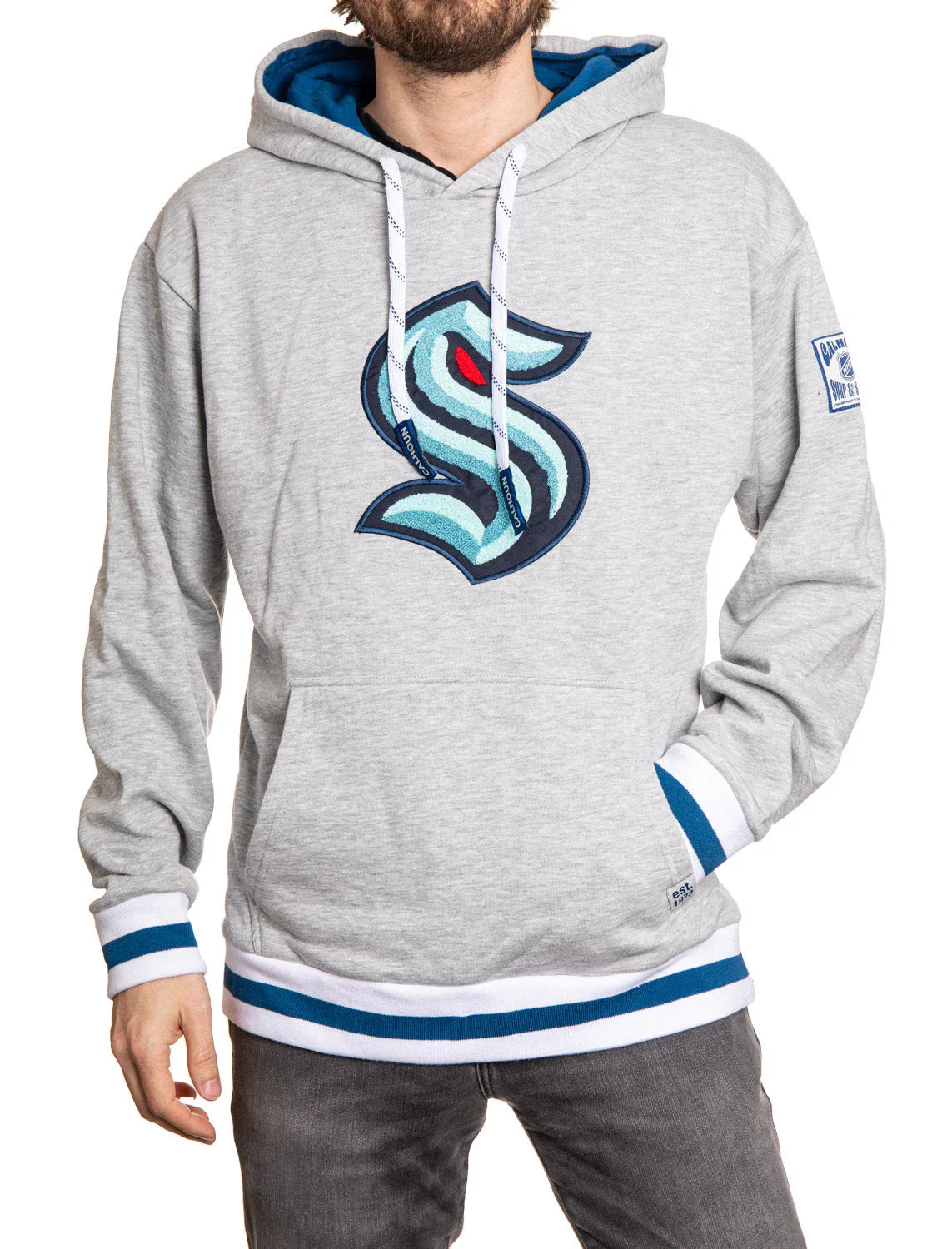 Man wearing grey Seattle Kraken chenille logo hoodie with blue and white striped cuffs