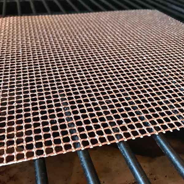 Copper mesh grilling screen on a barbecue grill, ideal for smoking and drying food.