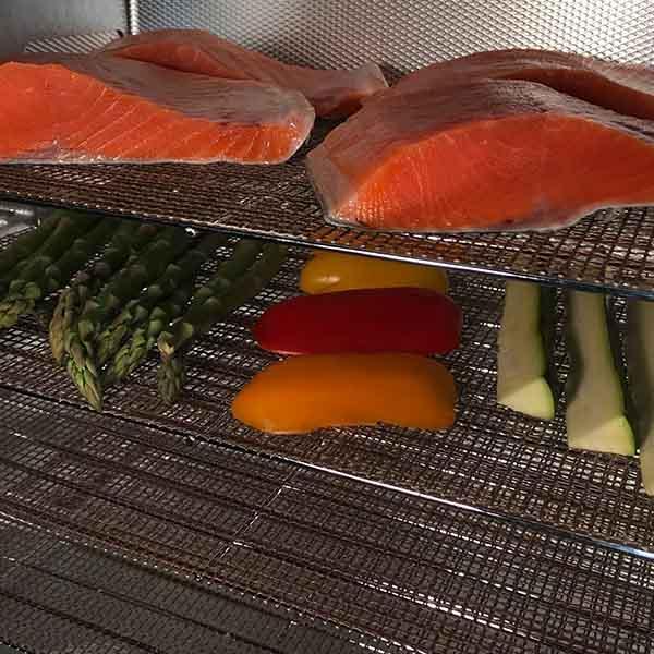 Salmon fillets and vegetables on stainless steel smokehouse drying grilling screens