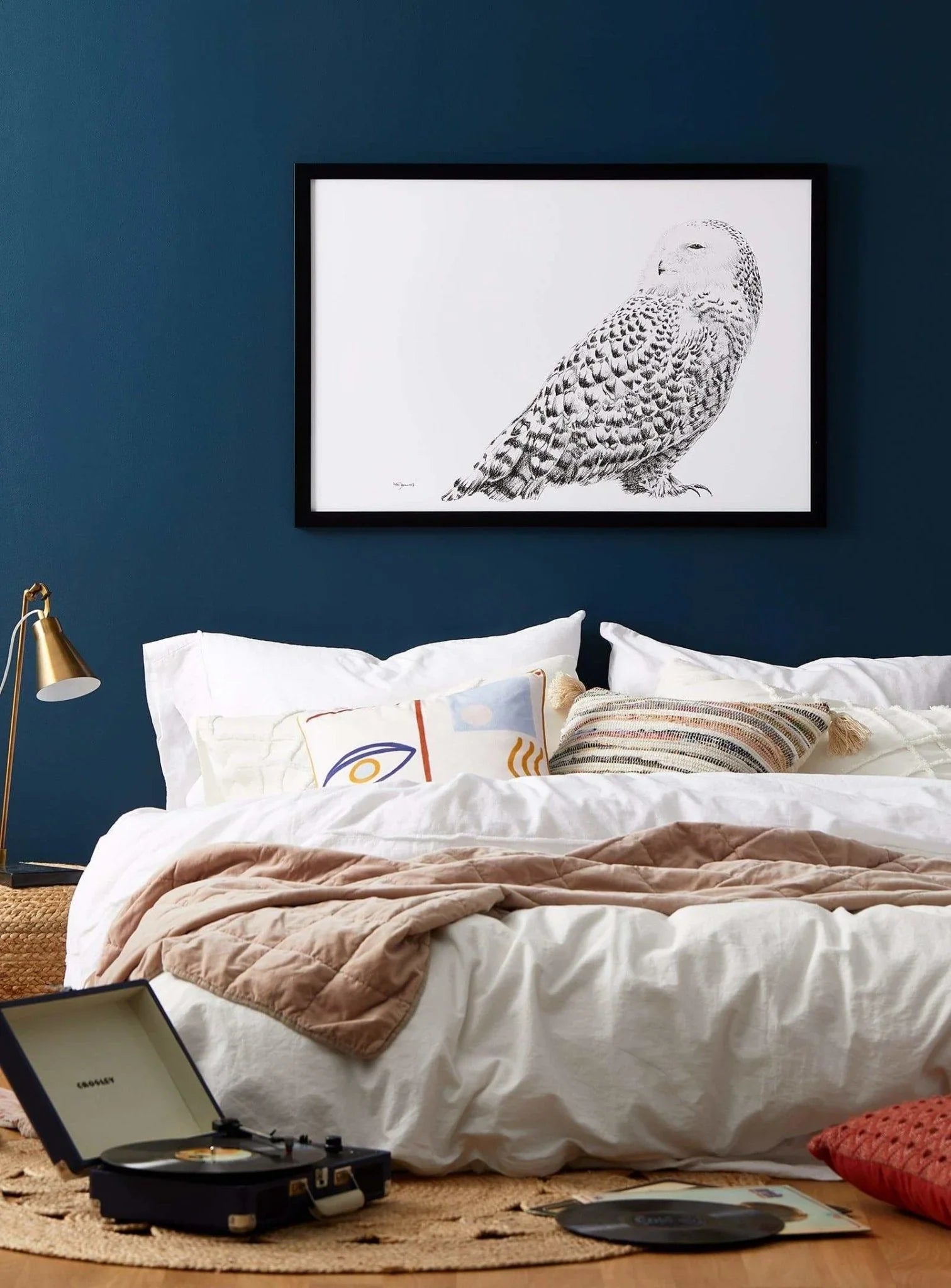 Cozy bedroom with white bedding, modern pillows, snowy owl art, and record player on floor