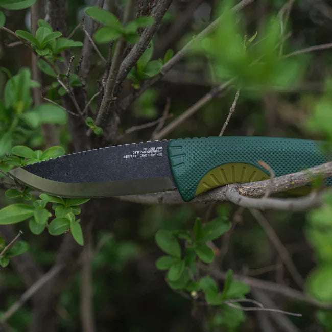 Outdoor survival knife with green handle in tree branches, bushcraft gear
