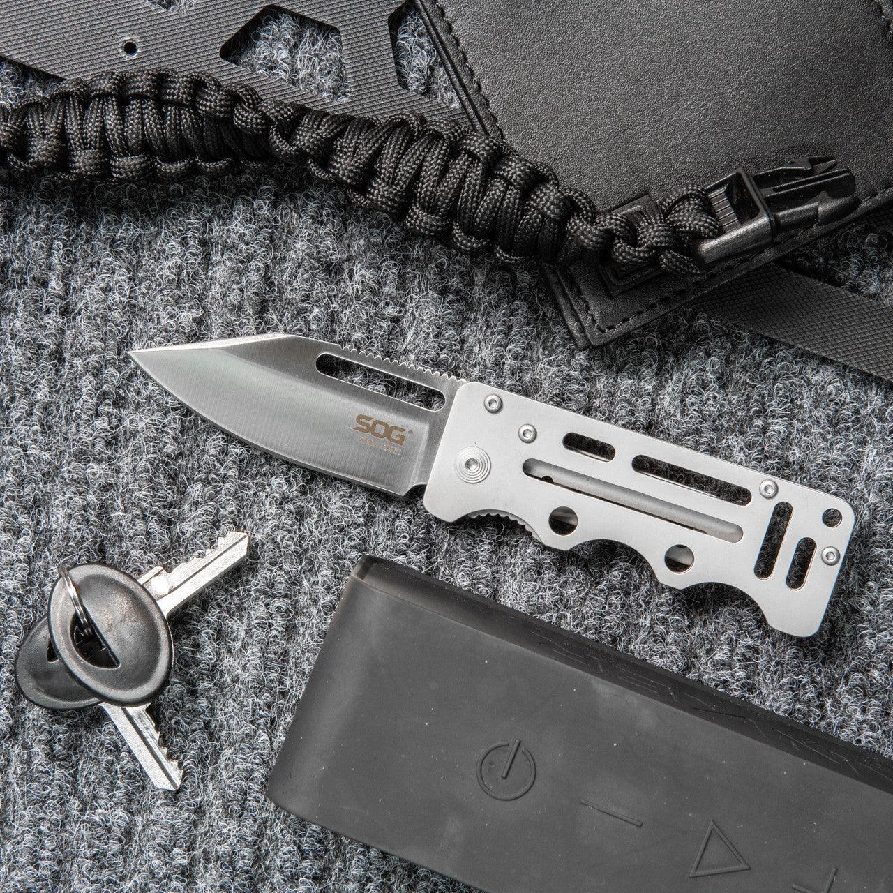 SOG cash card folding knife on grey knit surface with keys and black paracord