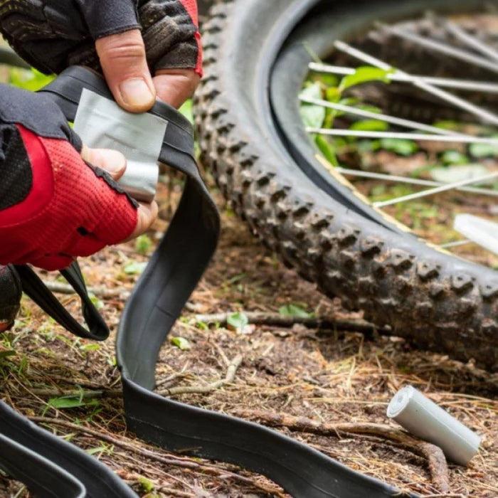 Person repairing mountain bike tire with duct tape outdoors on forest trail