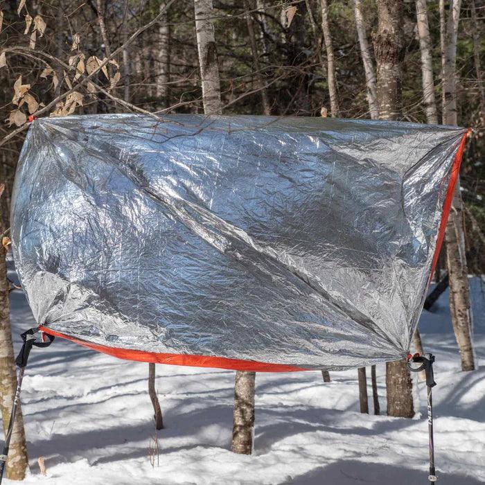 SOL emergency blanket tarp set up between trees in snowy winter forest outdoors