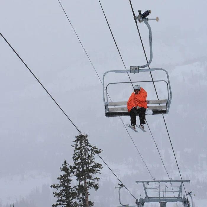 Skier in orange emergency blanket on snowy ski lift, winter mountain landscape