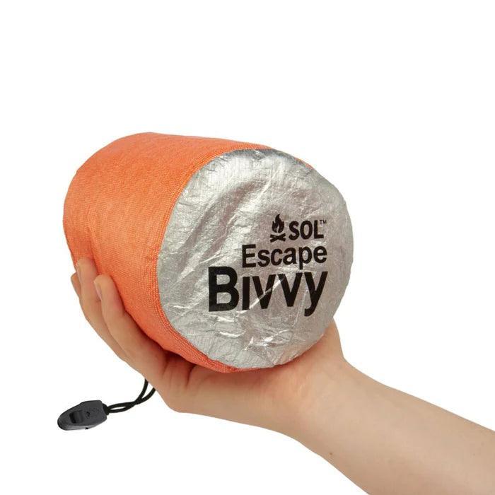 Hand holding orange SOL Escape Bivvy emergency survival sleeping bag
