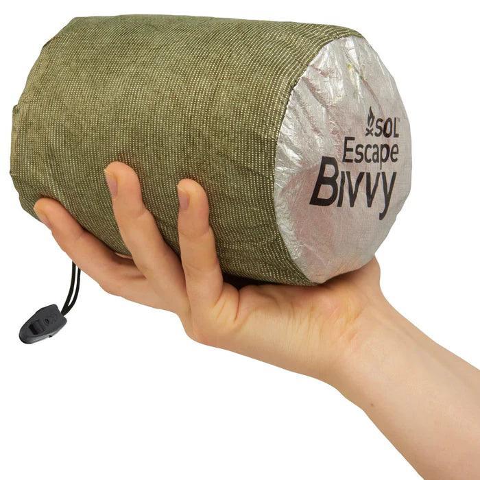 Hand holding compact SOL Escape Bivvy in green carrying sack, outdoor survival gear