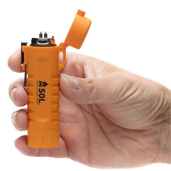 Hand holding orange SOL Fire Lite fuel-free lighter with flip top for outdoor use