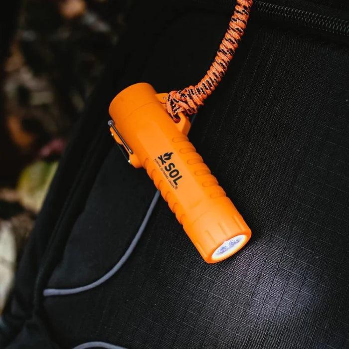 Orange SOL Fire Lite Fuel-Free Lighter clipped to a black backpack for outdoor use.