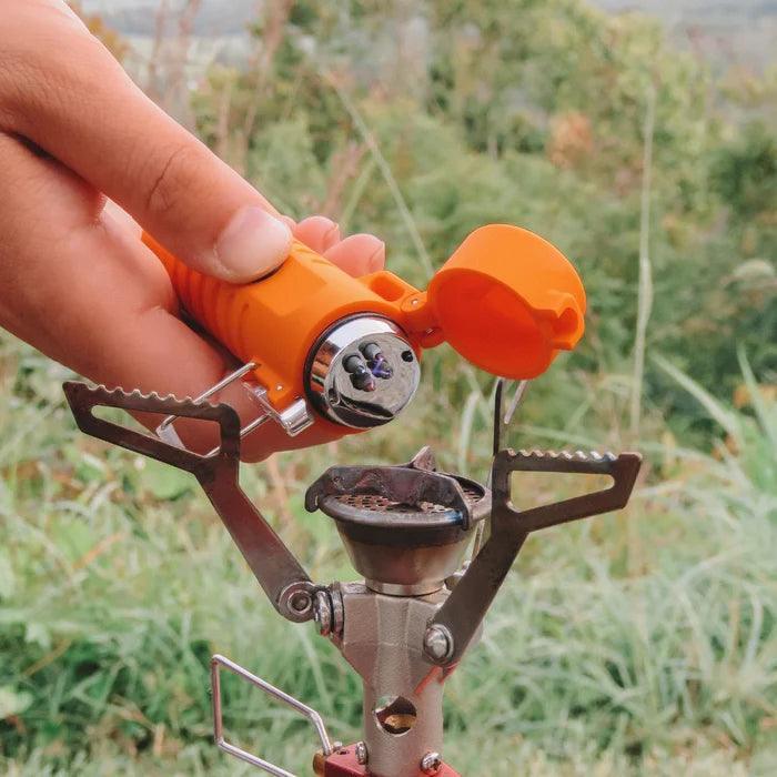 Hand holding orange arc plasma lighter above portable camping stove outdoors