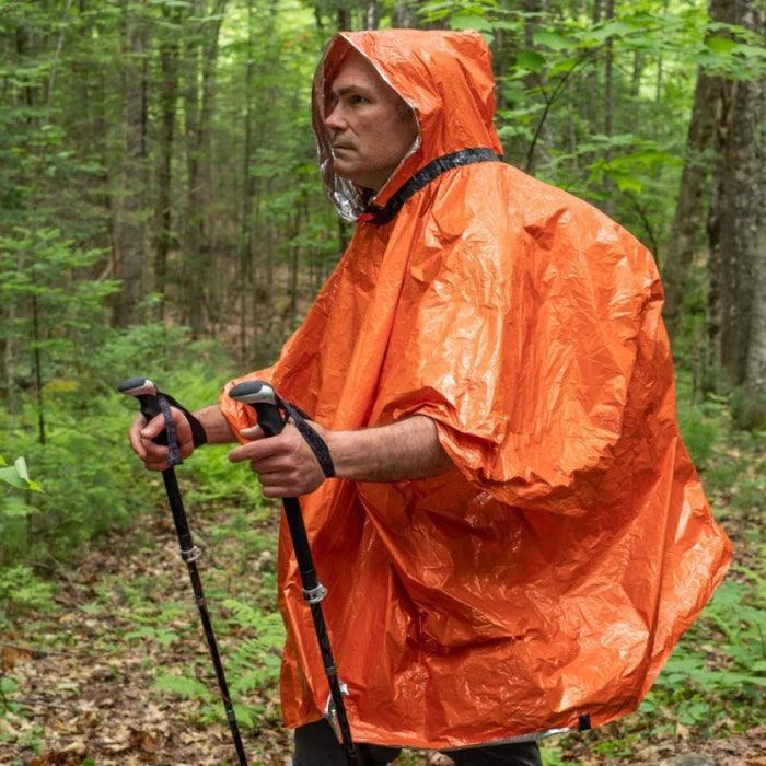 Man hiking in forest wearing orange heat reflective poncho with trekking poles