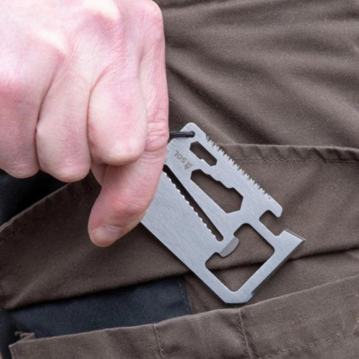 Hand holding SOL PackIt survival card multitool above brown pants pocket