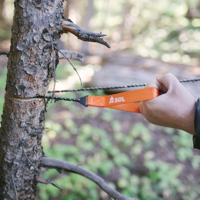 Hand using SOL pocket chain saw to cut tree outdoors in forest setting