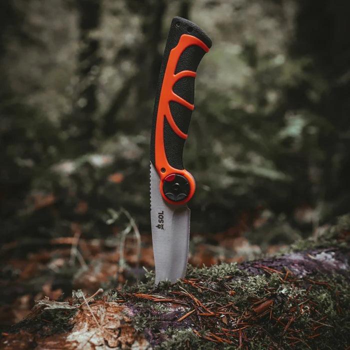 SOL folding saw with orange and black handle stuck in a mossy log outdoors
