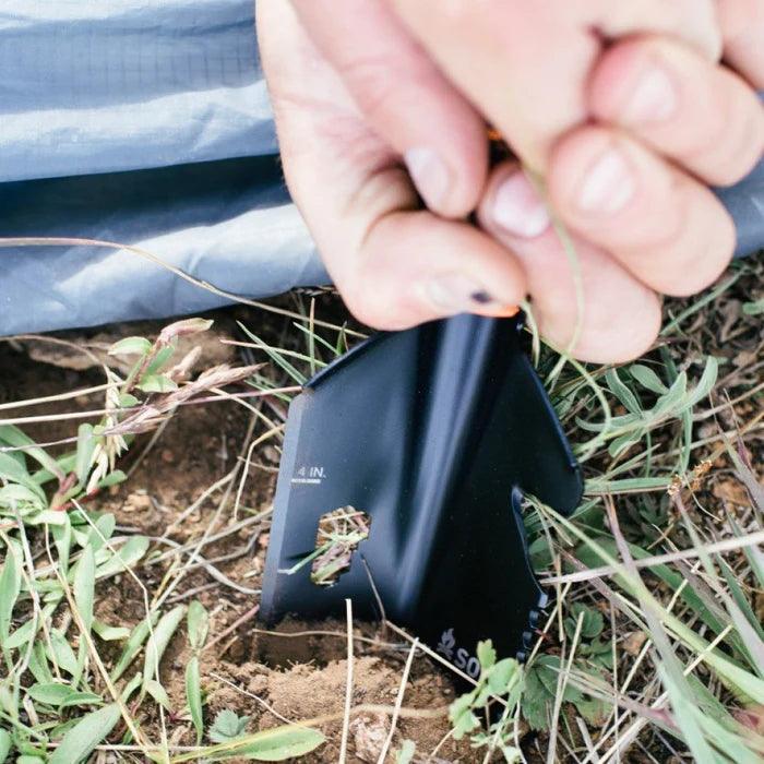 Hand using a compact black outdoor shovel to dig soil among grass and plants