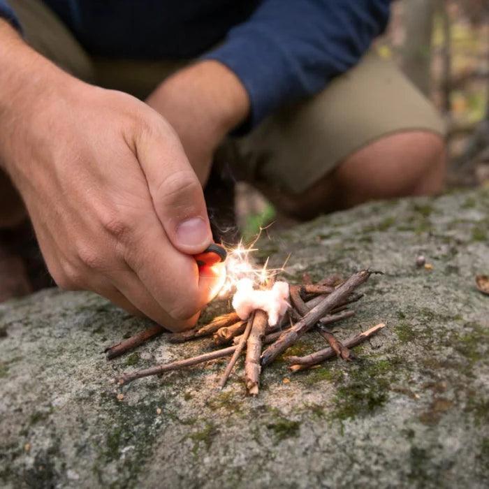 Person using fire starter to ignite tinder and twigs on a rock outdoors, camping scene