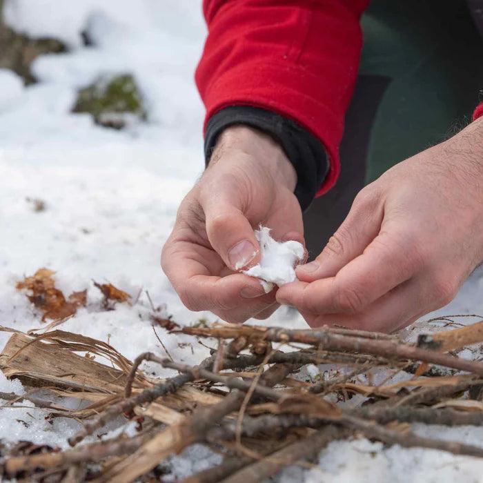 Person in red jacket preparing fire tinder with cotton and kindling outdoors in snow.