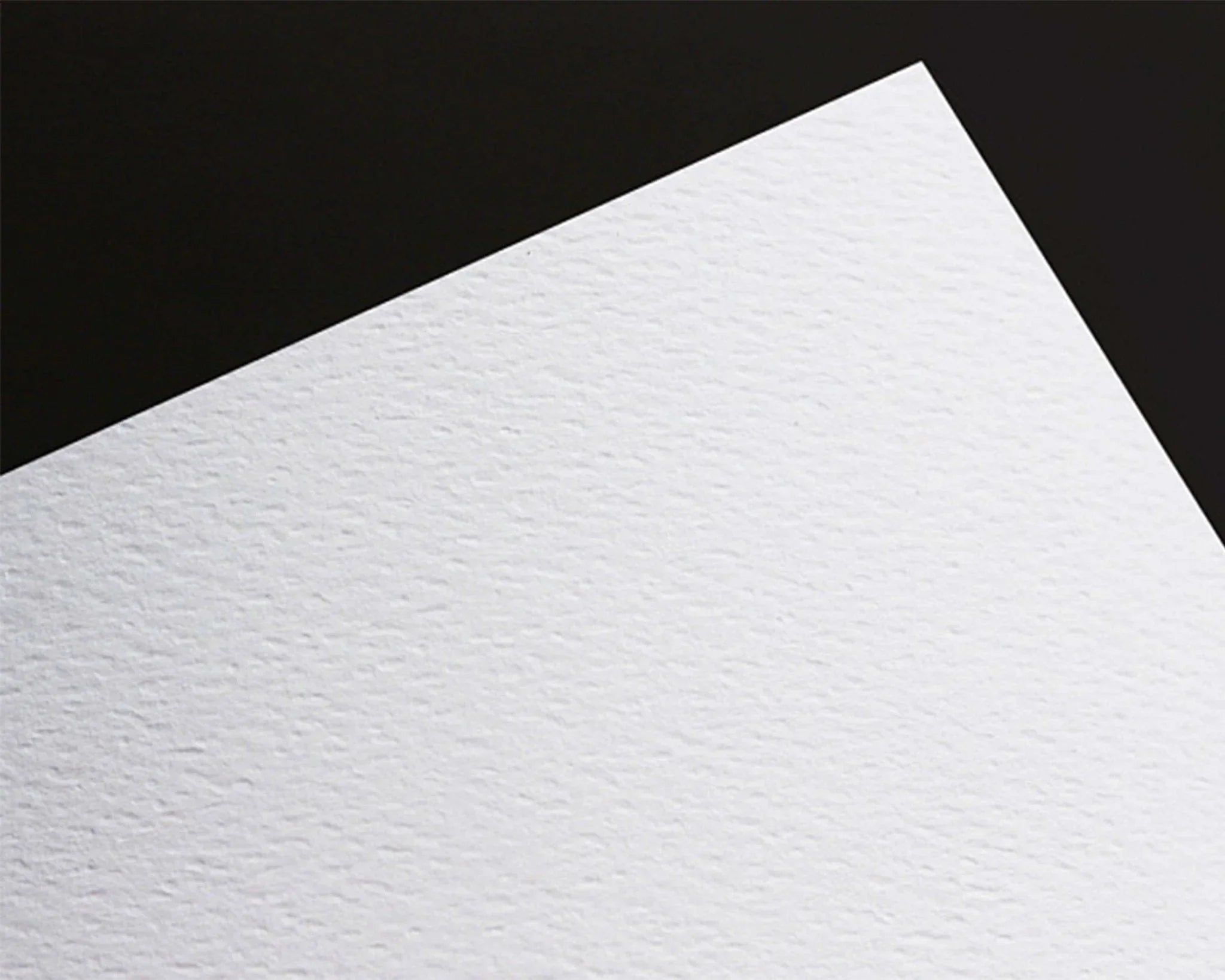Close-up of textured white cardstock paper with diagonal shadow on black background