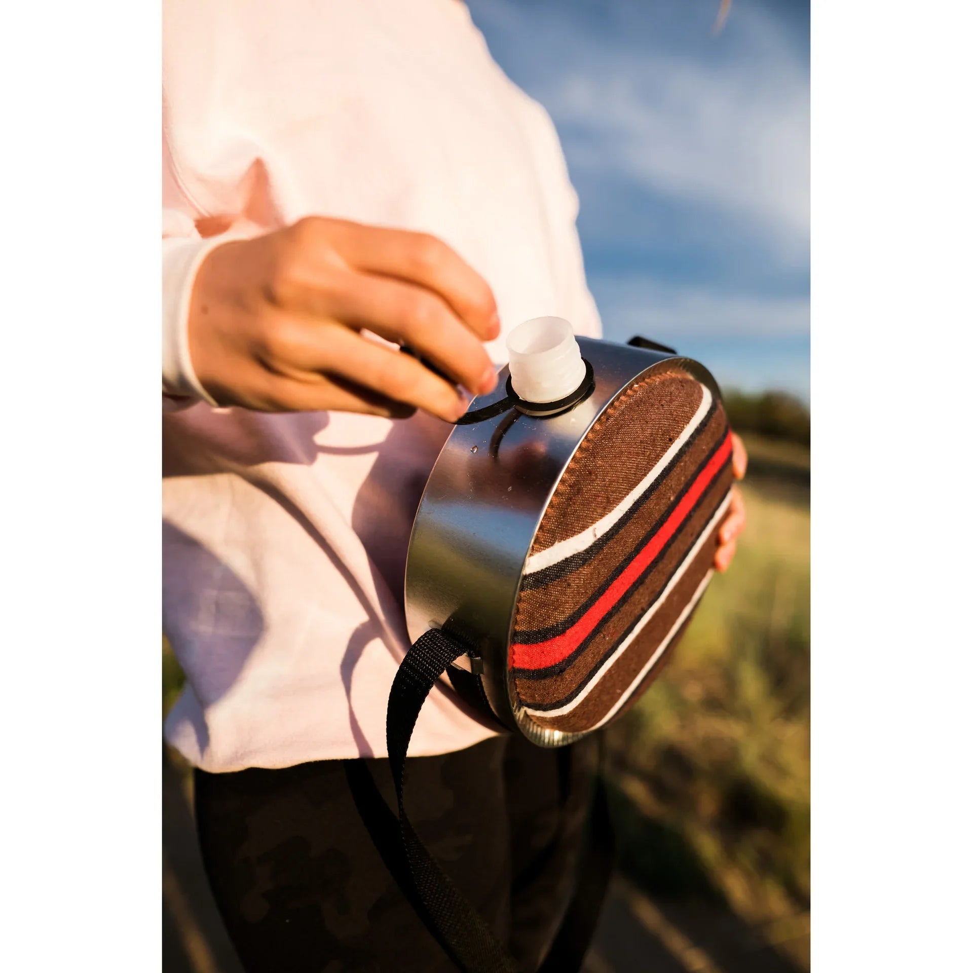 Person holding striped canteen outdoors, stainless steel flask with fabric cover
