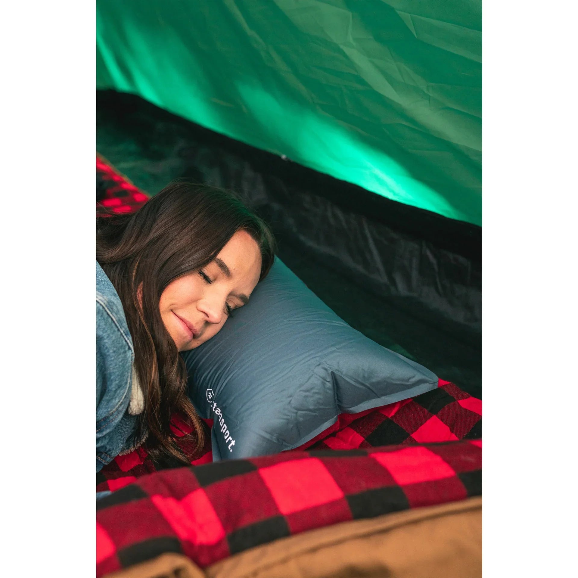 Woman sleeping on a gray Klymit pillow in a tent with a red plaid blanket, camping scene