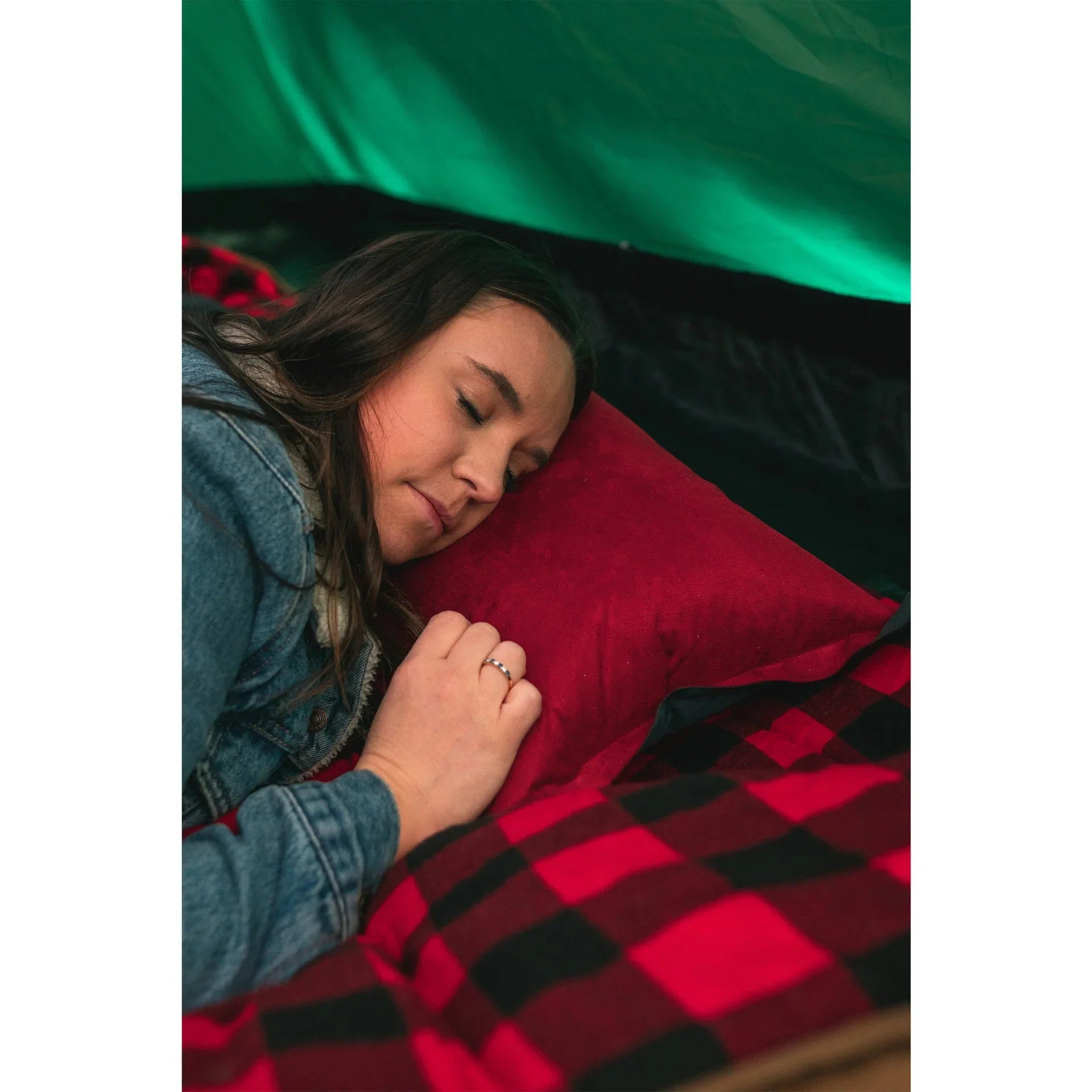 Woman sleeping on red pillow and plaid blanket inside tent, cozy camping scene